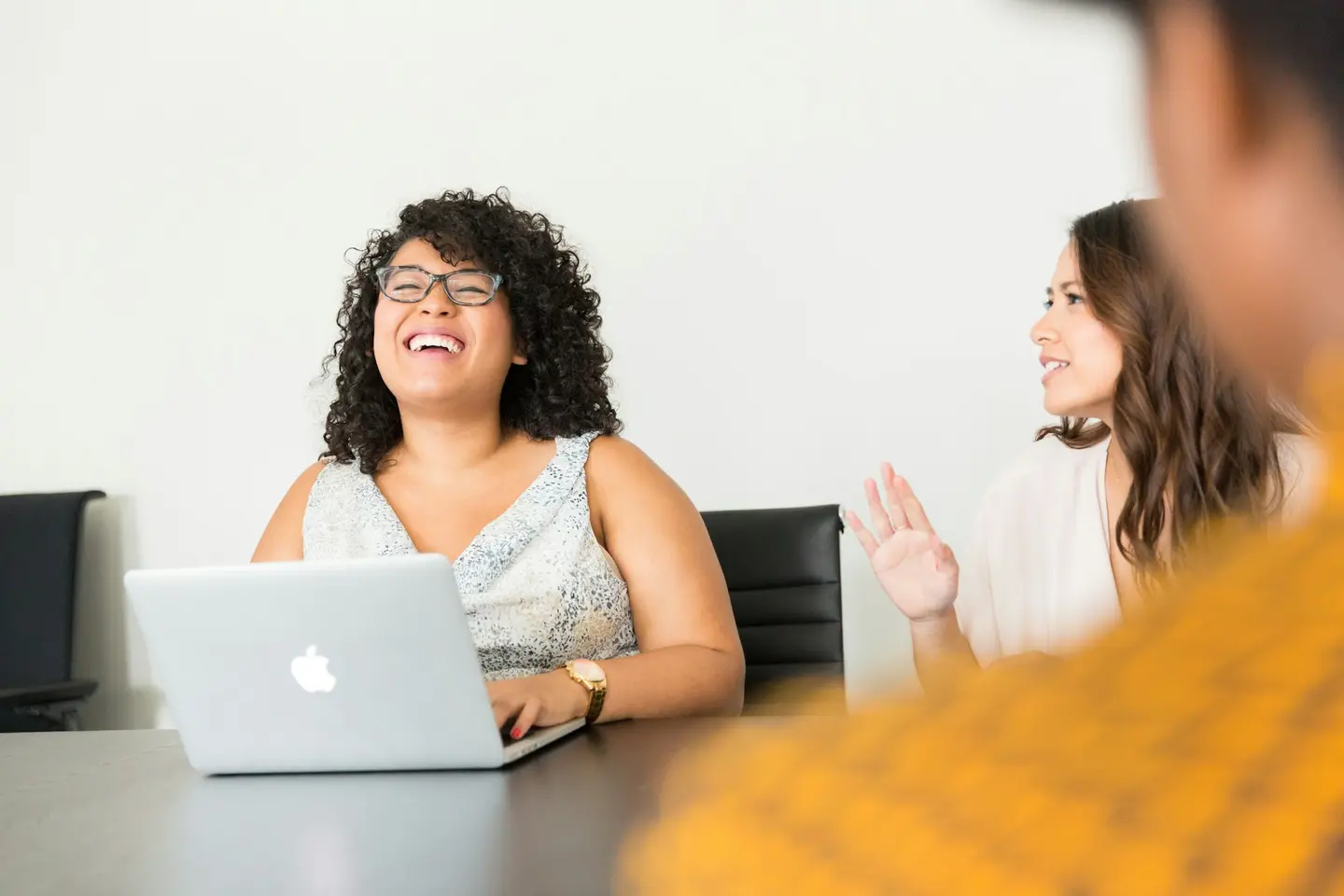 Dos profesionales conversan sonrientes frente a una computadora portátil en una oficina.